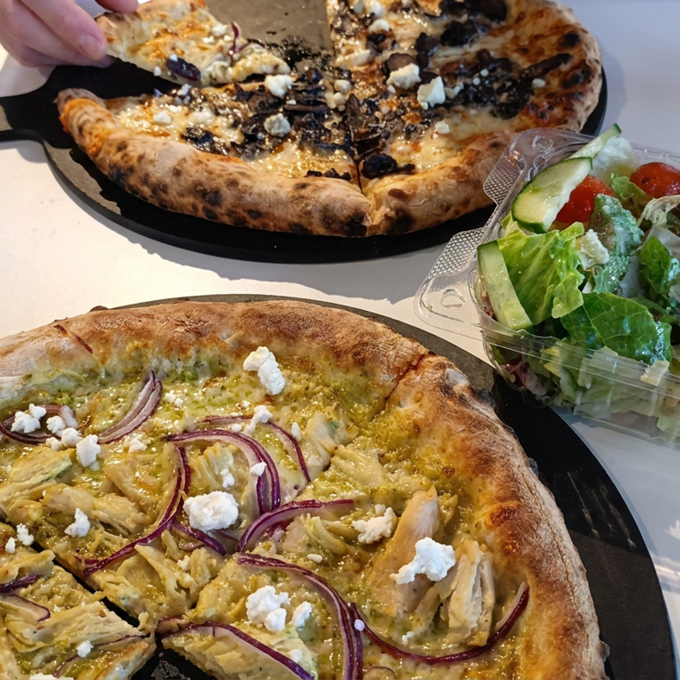 Two wood-fired pizzas with vegetables, chicken, red onion, and crumbled cheese served alongside a fresh garden salad.