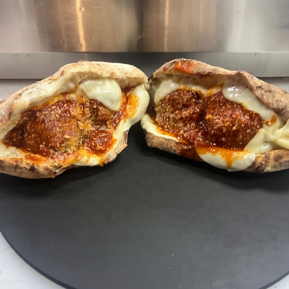 Two toasted pita sandwiches filled with meatballs, melted cheese, and tomato sauce on a black serving board.